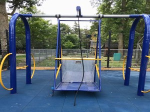 playground equipped with blue and yellow wheelchair swing with rubber matting underneath 